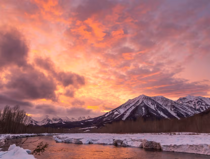 Snowy mountains and river reflecting a vivid orange sunset.
