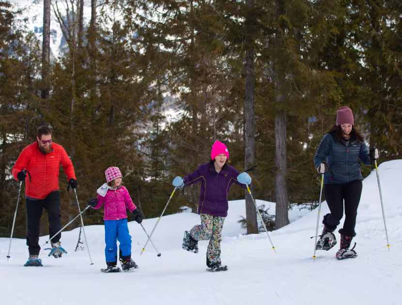Two adults and two children snowshoeing in a winter forest at Fernie Alpine Resort