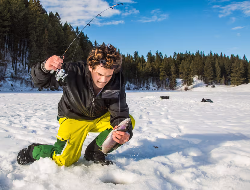 A man kneeling down on a frozen, snow-covered lake, holding a trout