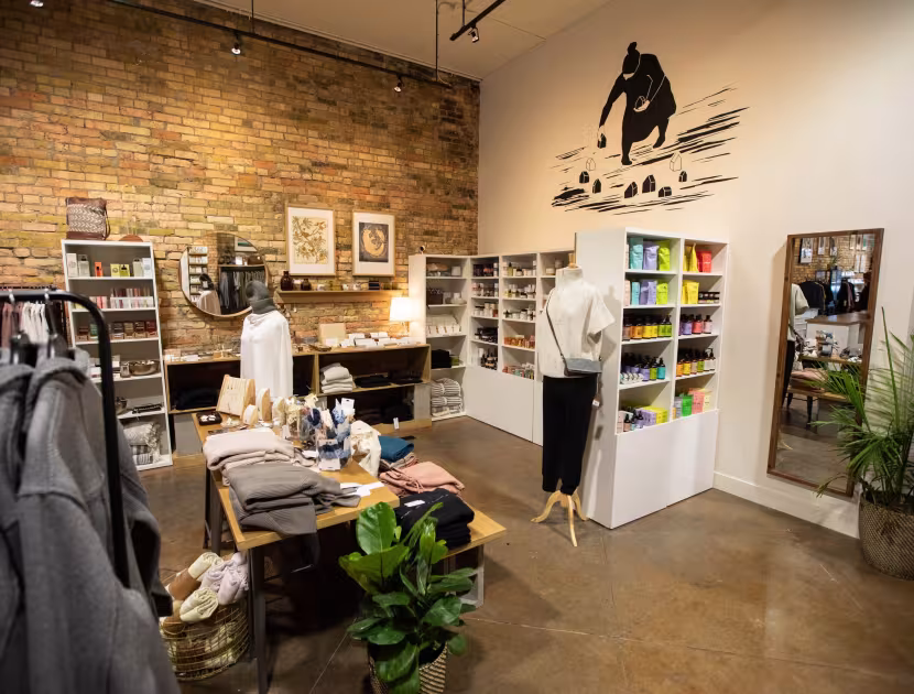 Store interior with brick wall, clothing racks, table, mannequin, and plants.
