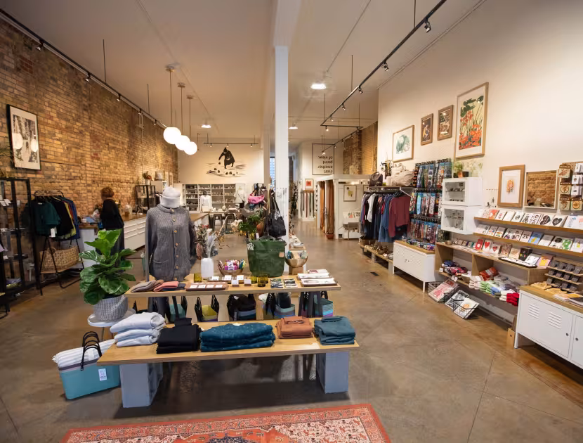 Cozy store interior with clothing, shelves, and plants on concrete floor.
