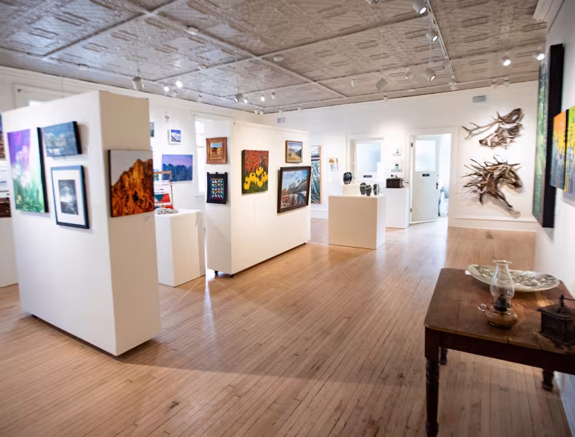 An art gallery with paintings on walls and wooden table.