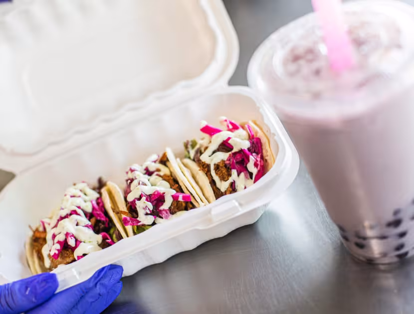 Hand holding a white takeout container with waffles; boba tea beside it.