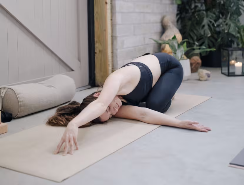 Woman in yoga pose on mat, leaning forward with arms extended.