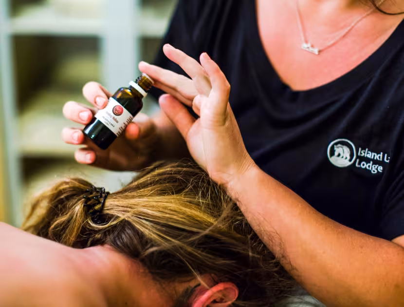 A person in a black shirt with an Island Lake Lodge logo applying oil to another woman's hair.