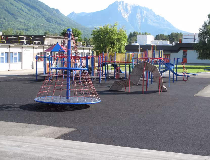 Playground with colorful climbing structure and swings, set against mountains.
