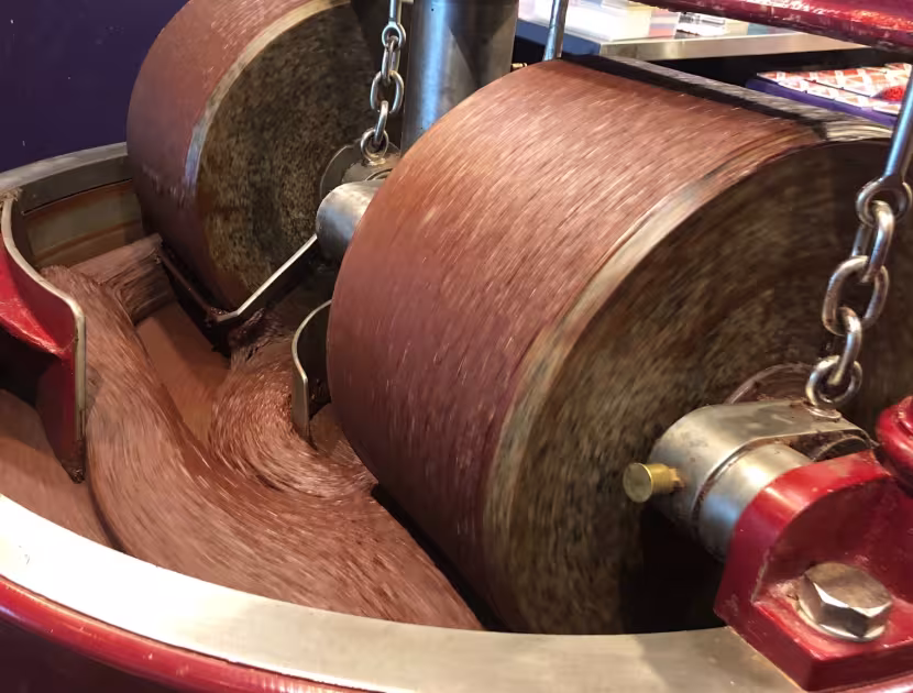 Two large brown cylindrical rollers with chains, in a red and silver machine.