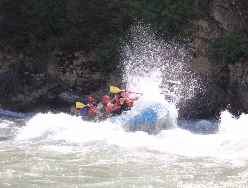 People in orange life jackets on a blue raft navigating rough water.