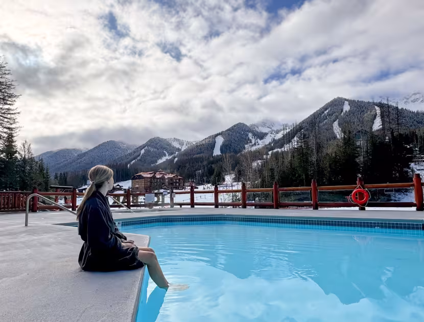 Woman sitting by outdoor pool with snowy mountains in background.