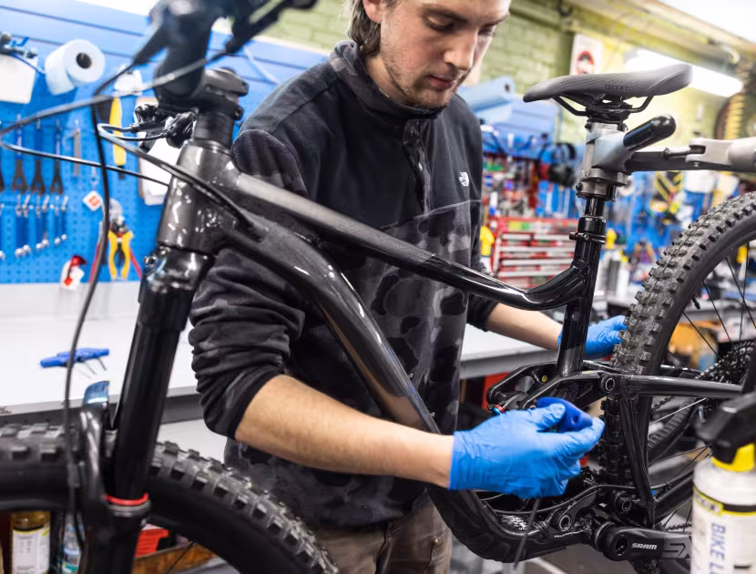 Man in a workshop, wearing blue gloves, repairing a black bicycle.