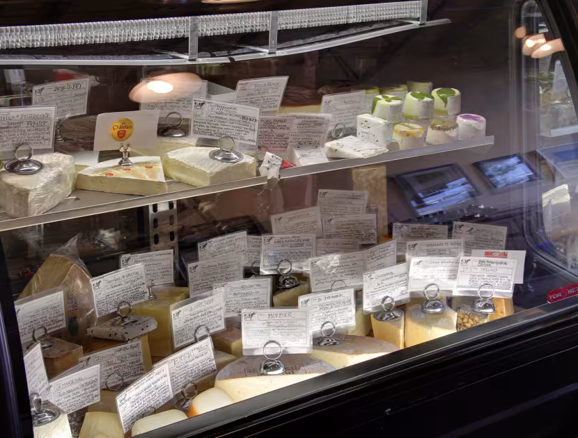 Curved display case filled with assorted cheeses and labeled trays.