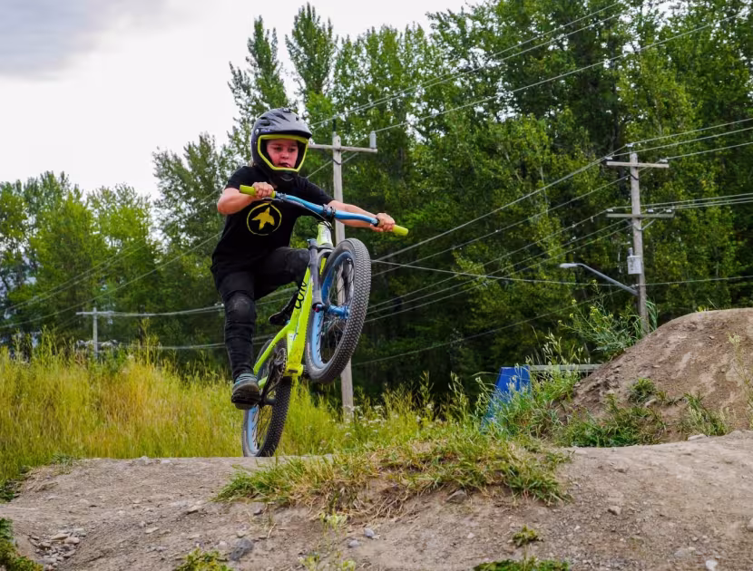 Bicyclist in black gear and red helmet jumps over dirt mound on a neon green bike.