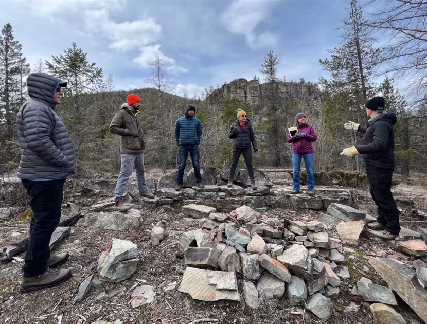 A group of people standing in a circle on rocky terrain at Silver Springs near Fernie, surrounded by trees and a blue sky.